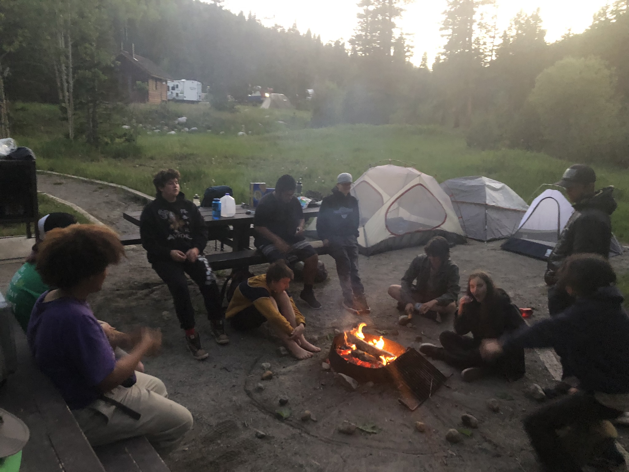 Students sitting around a campfire in front of tents.