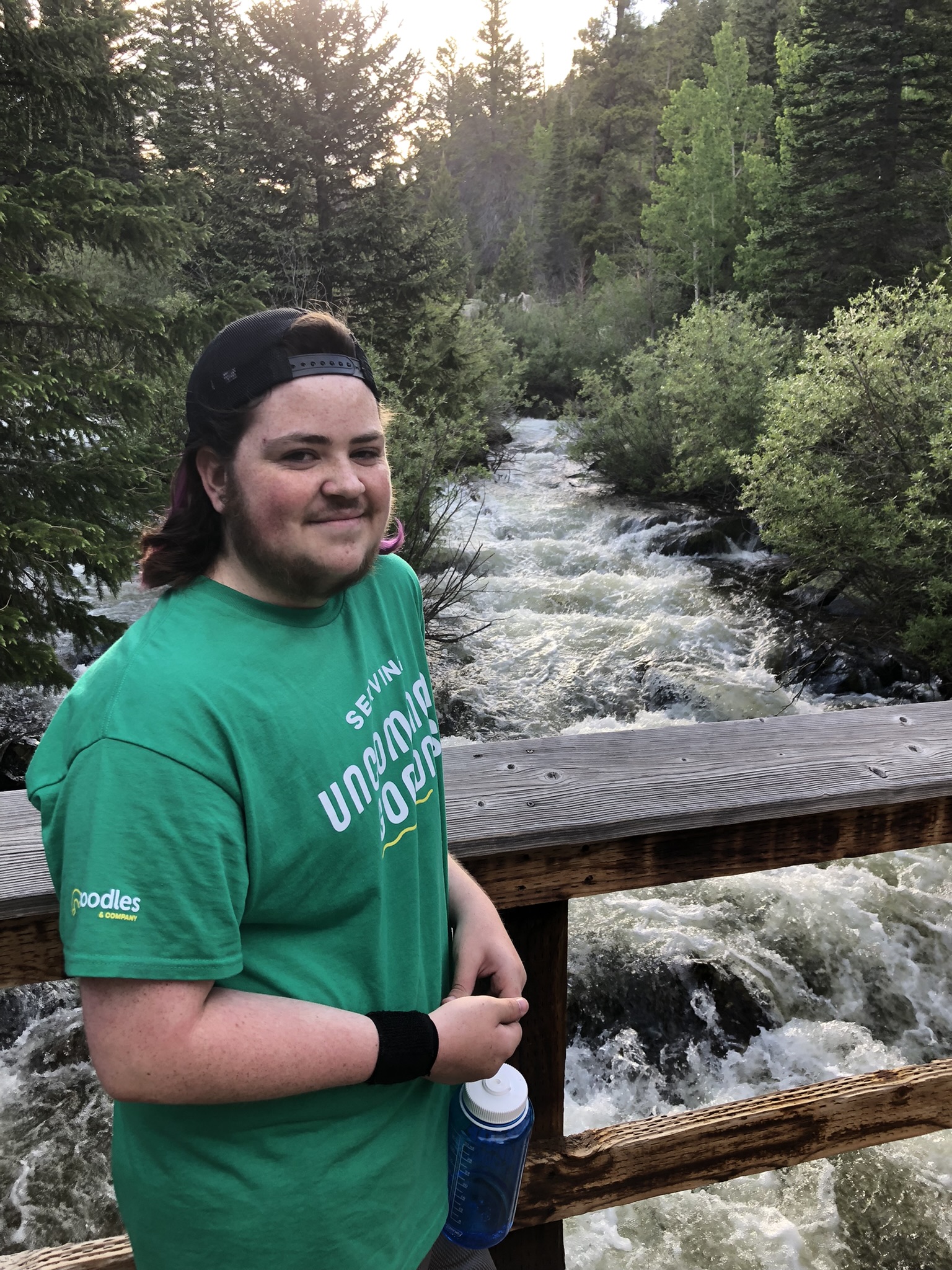 Student standing on a bridge over a creek smiling.