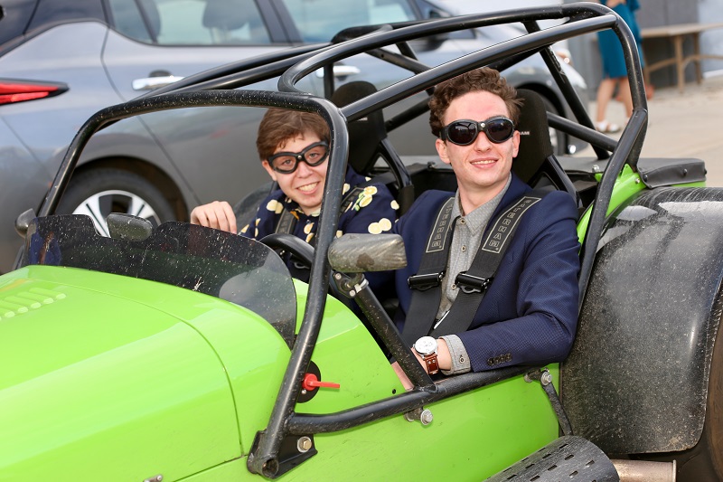 Two boys sitting in a two seat Caterham roadster wearing old style aviator goggles.