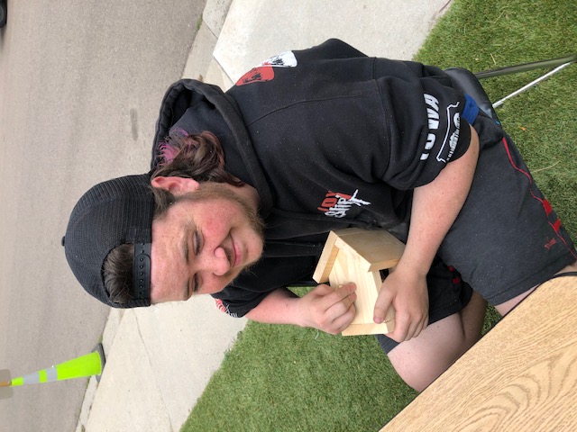 Student smiling while building birdhouse.