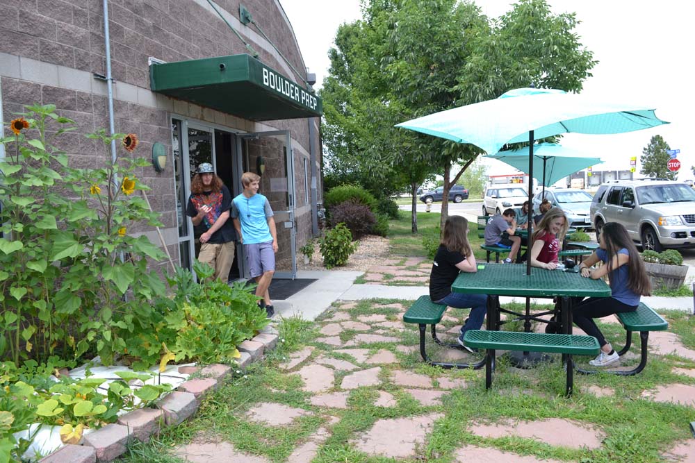 Students sitting at picnic tables in school front patio area.