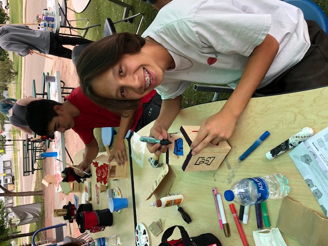 Students smiling while working to add color to a birdhouse using a marker.