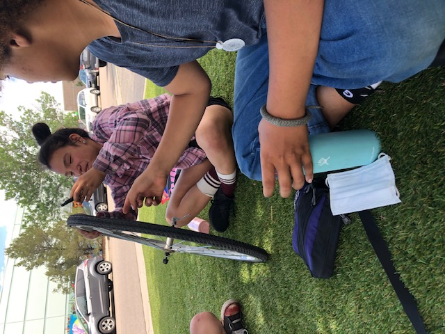 Student using bike tire levers to remove tire from rim to repair a flat tire.